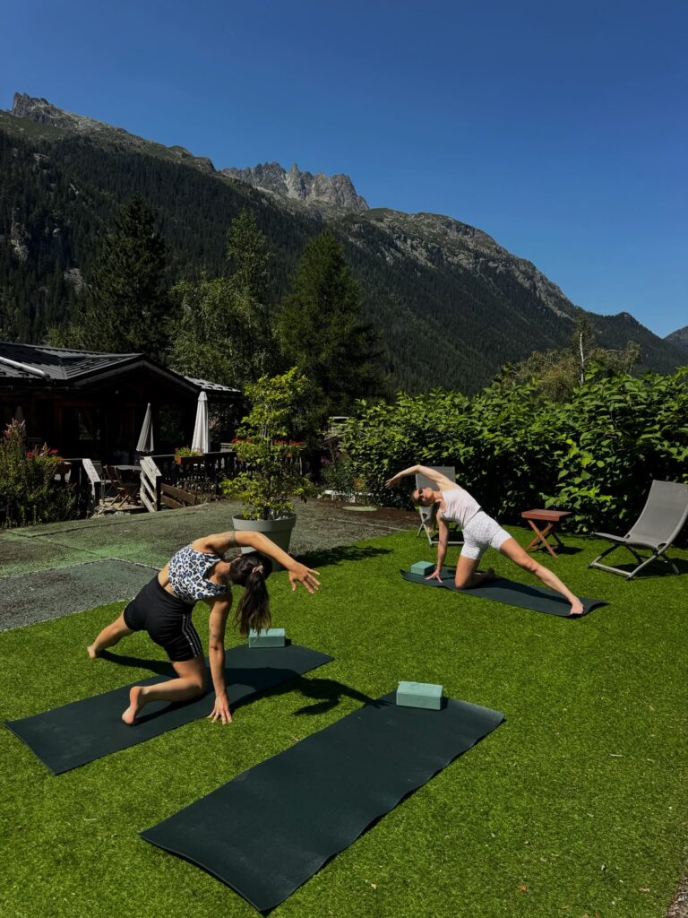 Cours de yoga collectif en plein air à Chamonix, deux participantes dans le jardin de l’Hôtel Jeu de Paume face aux Aiguilles